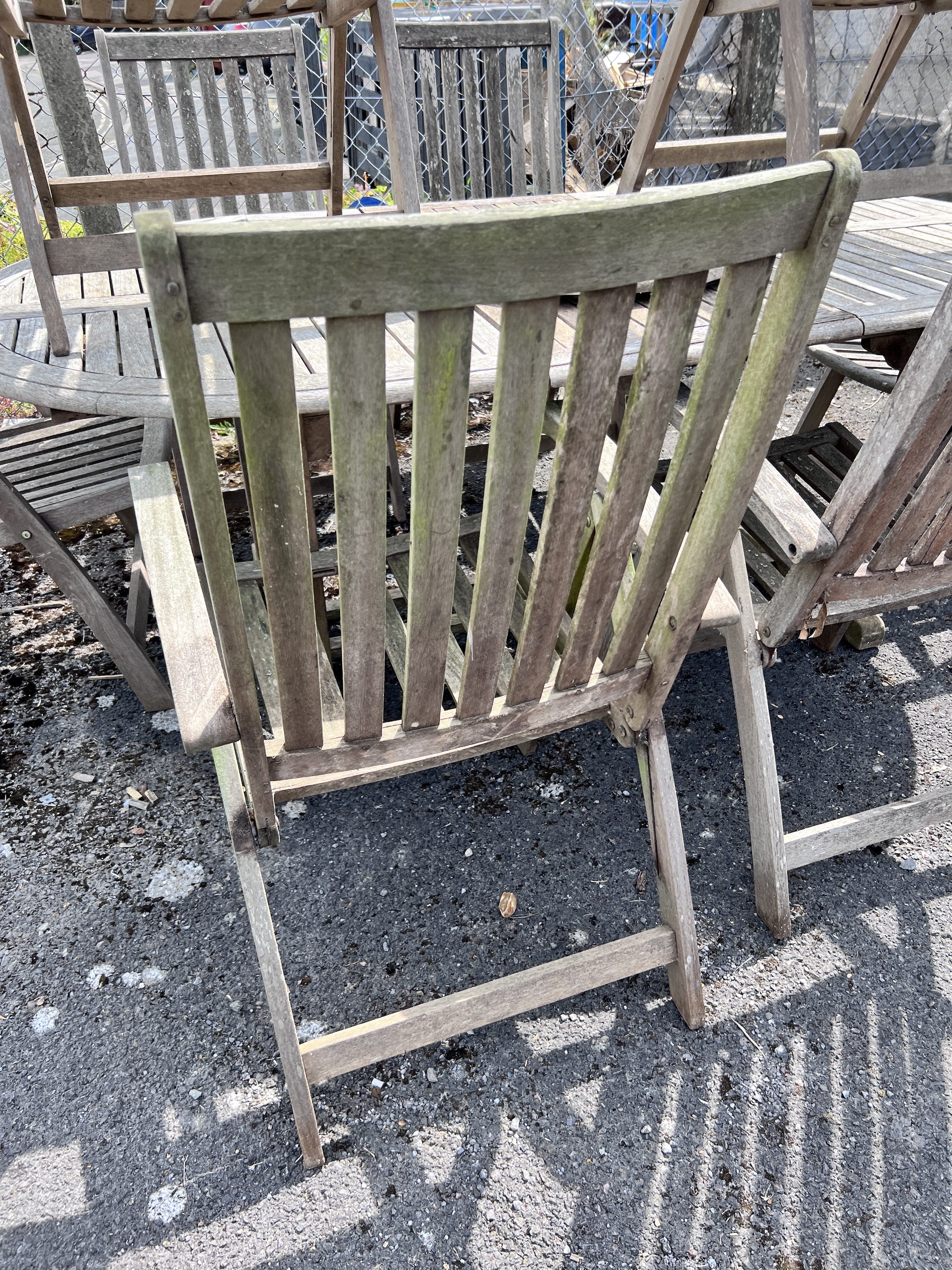 A weathered teak oval extending dining table and eight folding elbow chairs (7 plus 1), table 208cm extended, depth 110cm, height 76cm